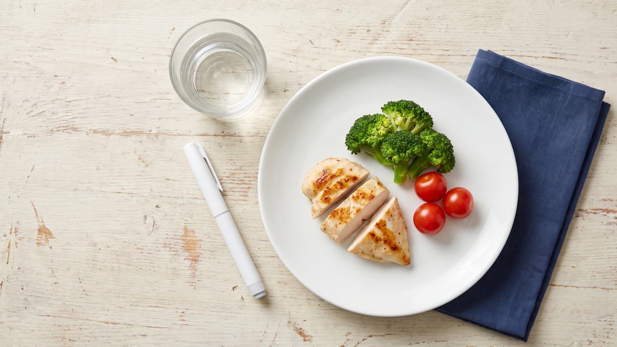 Plato con una porción pequeña de comida junto a una pluma inyectora genérica y una cinta métrica